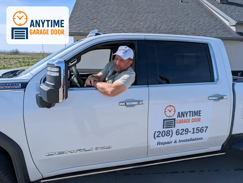 Team member in an Anytime Garage Door cap leans out the driver's window of a white pickup with the company door decal.