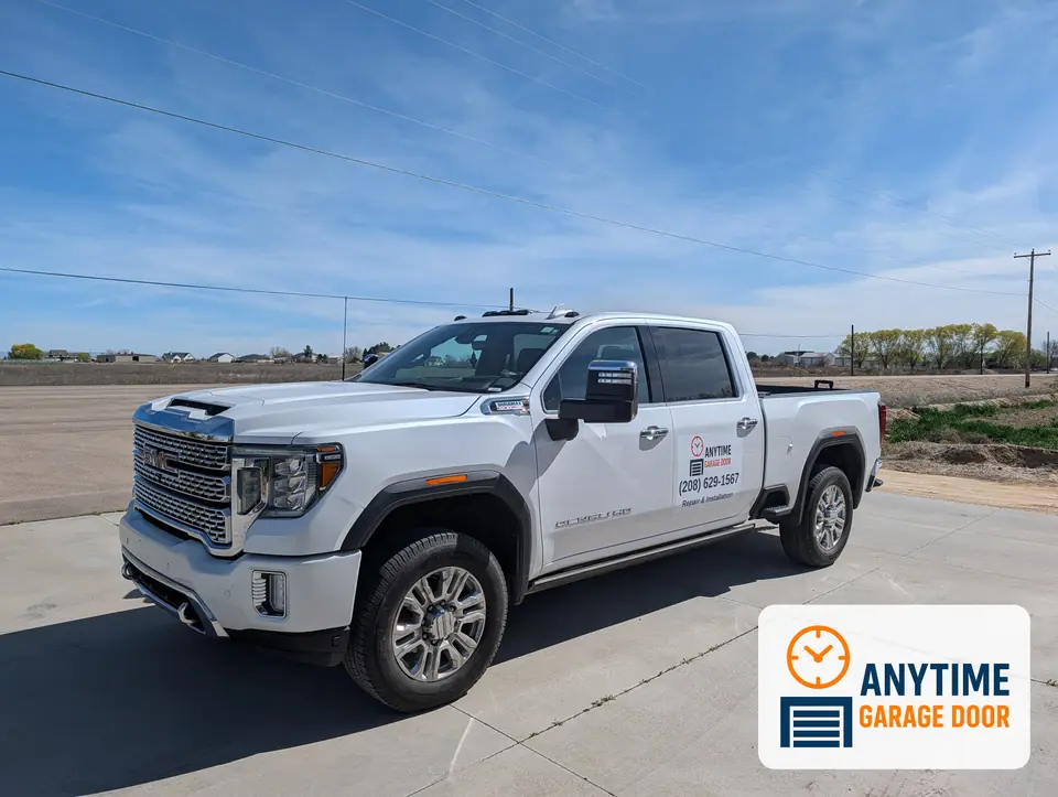White pickup truck with the Anytime Garage Door logo and phone number on the rear door, parked on a concrete pad.