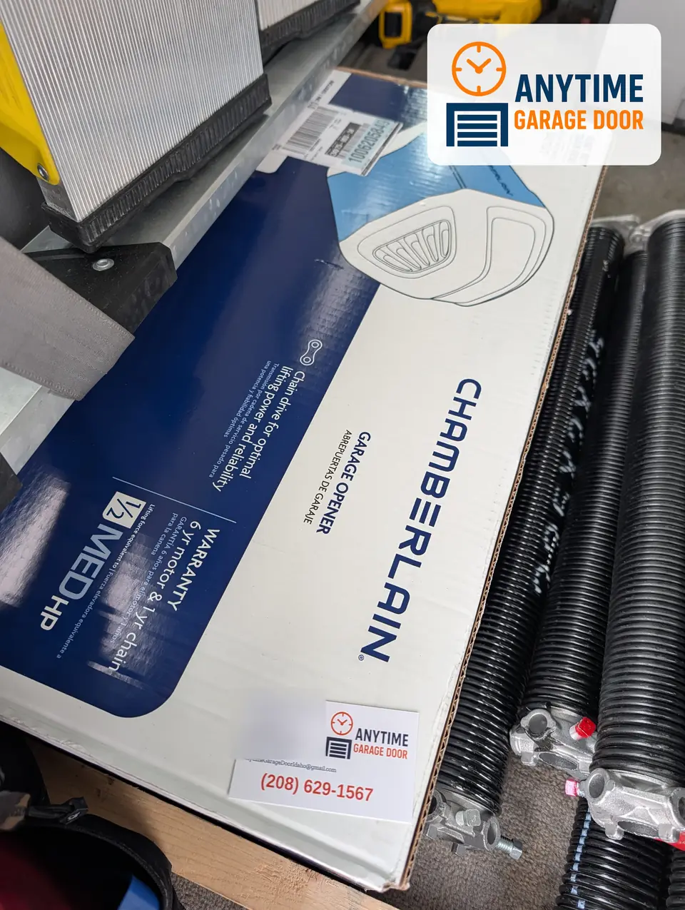 A boxed Chamberlain garage door opener beside a row of black torsion springs, with an Anytime business card on the box.