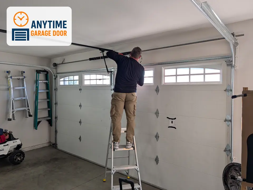Technician on a step ladder works on the torsion springs above a two-car garage door with arched windows.