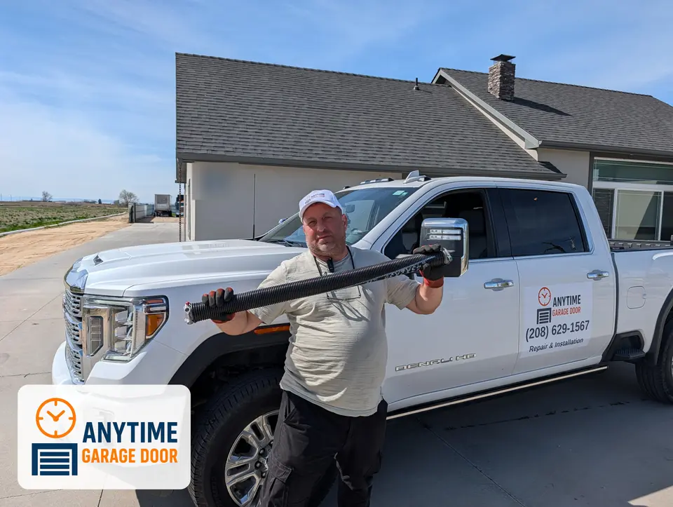 Man in an Anytime Garage Door cap holding a torsion spring in front of a white company pickup truck