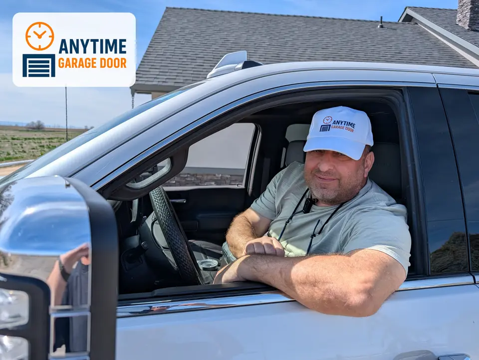 Man in an Anytime Garage Door cap resting his arms on the open window of a white pickup truck