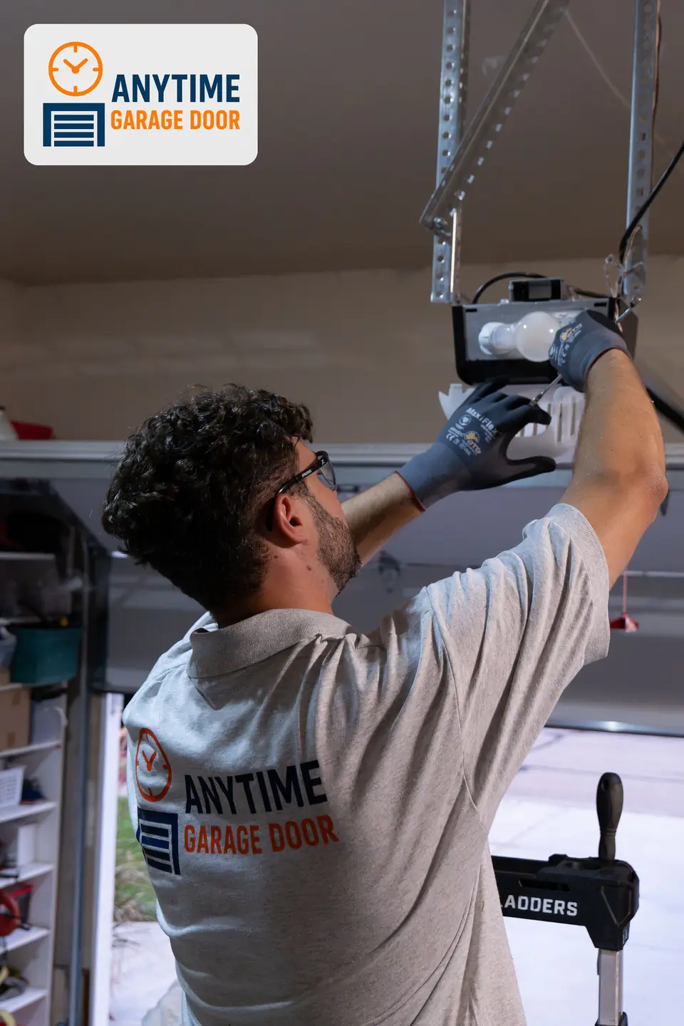 Technician in safety glasses works on the light cover of a ceiling-mounted garage door opener.