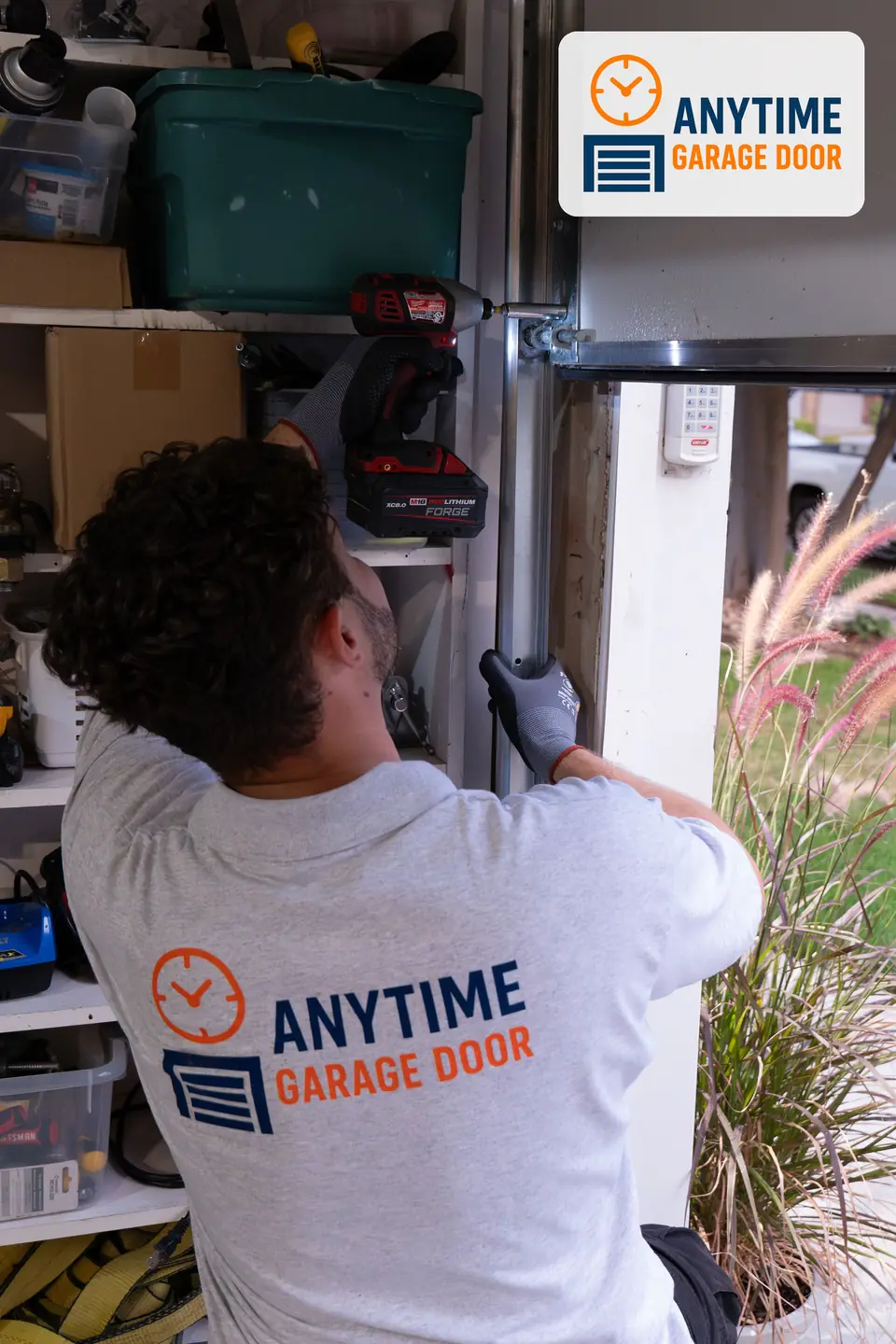 Technician holds a garage door's vertical track and tightens a bracket with a red impact drill.
