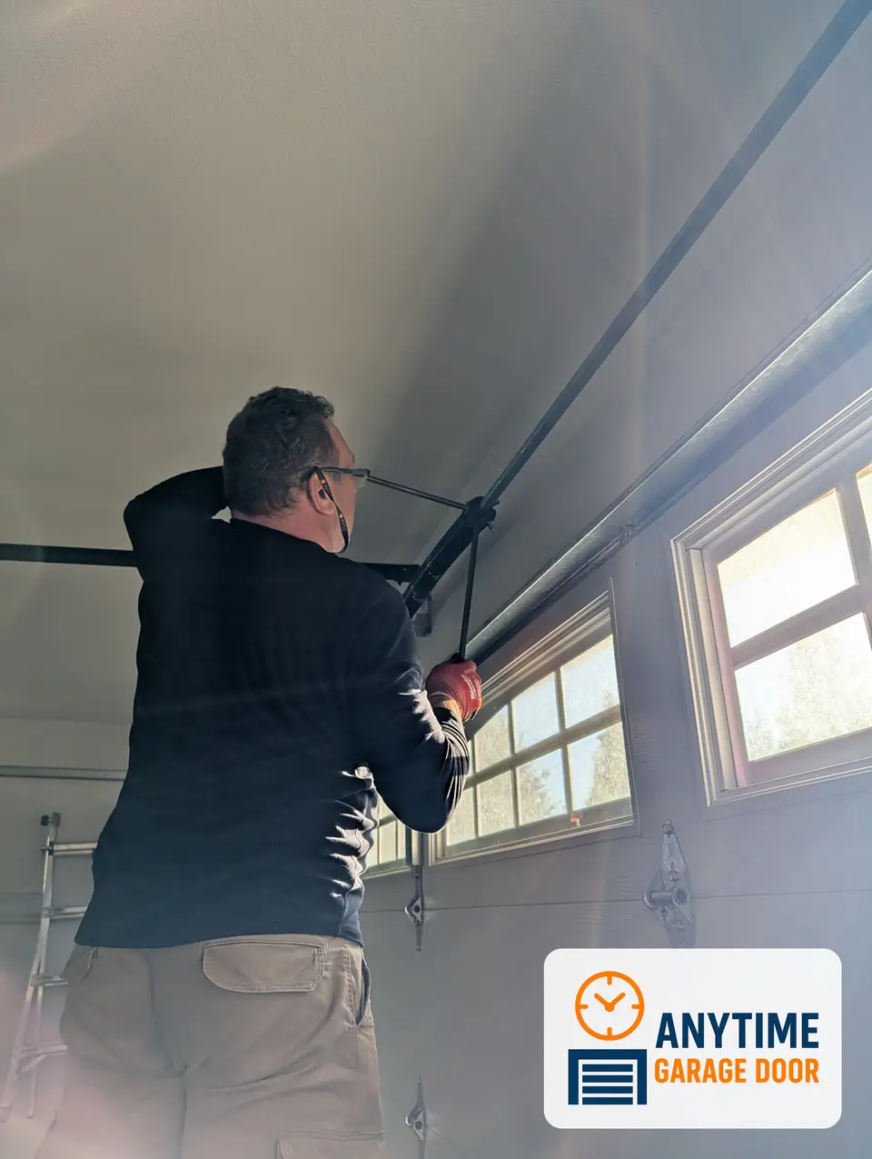 Worker using a winding bar on a torsion spring above a garage door with windows
