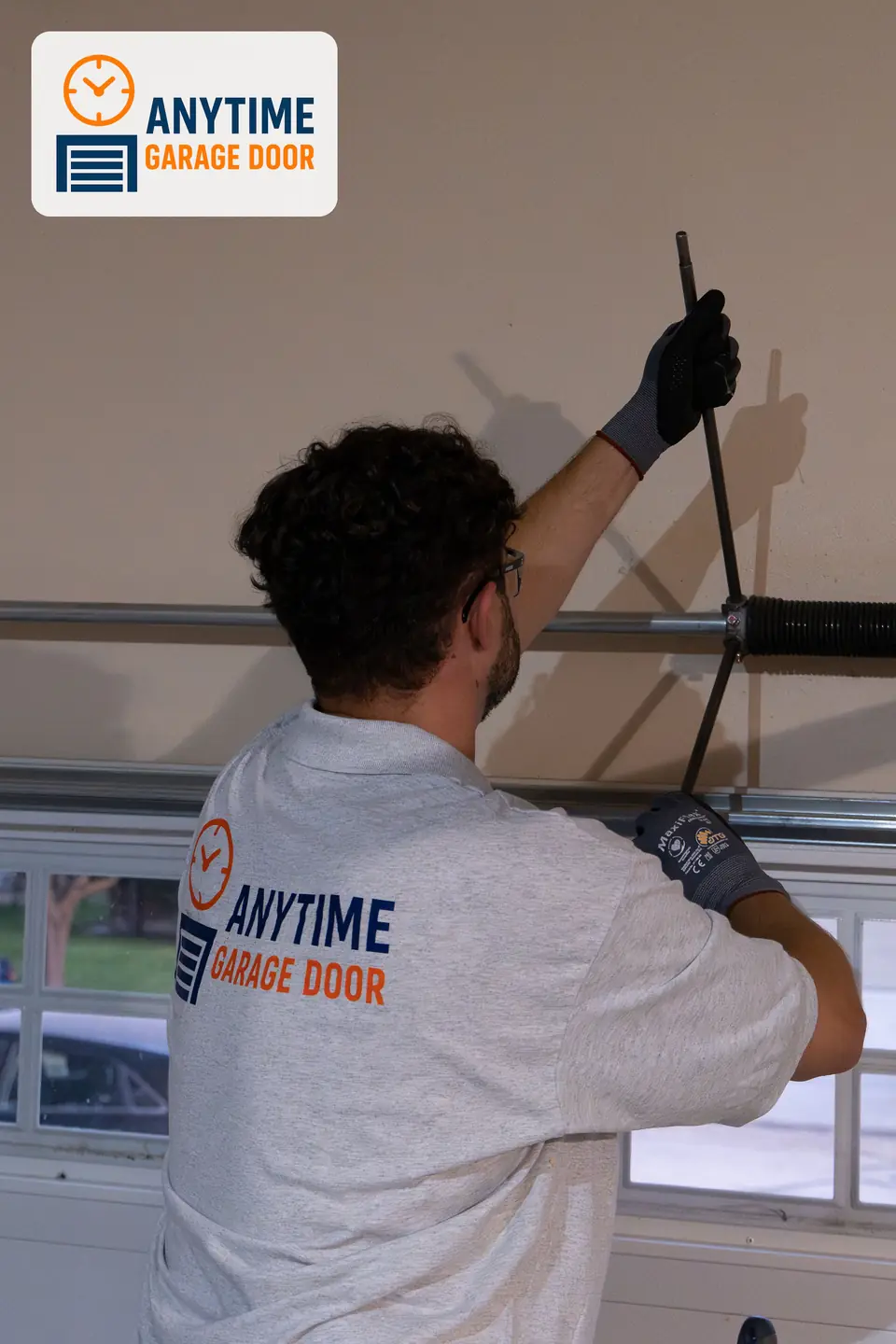 Technician in safety glasses holds two winding bars in a torsion spring cone above a garage door.