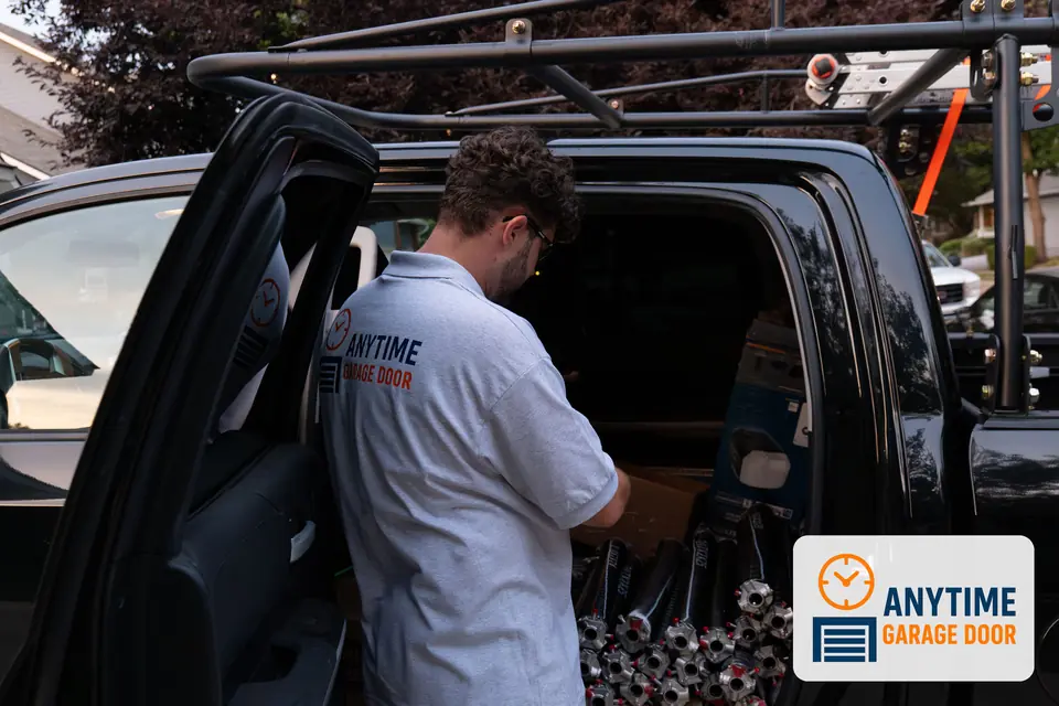 Technician in an Anytime Garage Door shirt reaches into the back seat of a black pickup stocked with torsion springs.